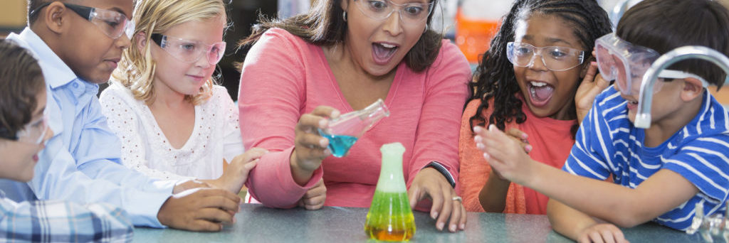 elementary school teacher and students in science lab, doing a chemistry experiment with colorful liquids in beakers.