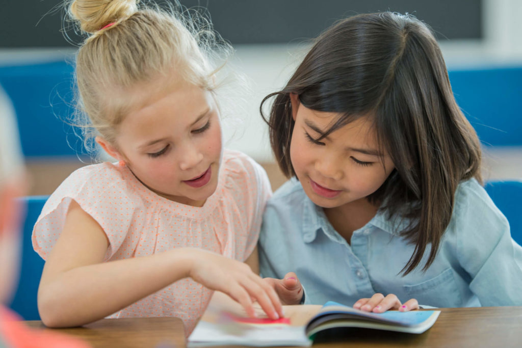 Two students read a non-fiction book together and practice reading strategies