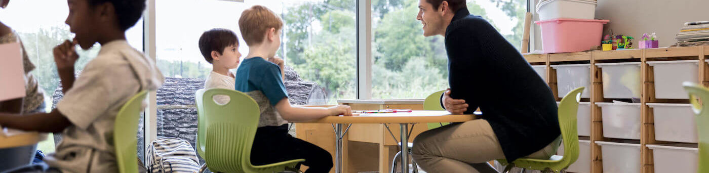 A teacher works with his students in a modern learning environment rather than standing at the front of the class.