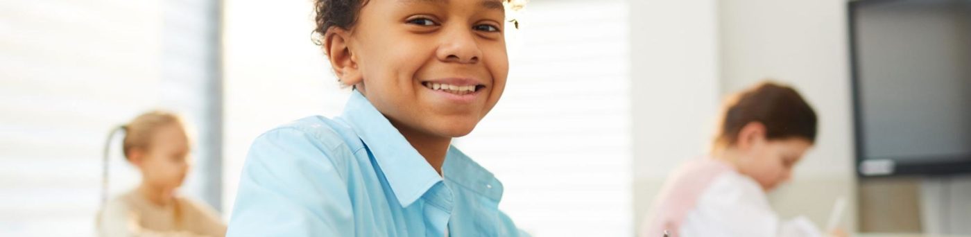 An ELL student smiles and writes in the classroom.