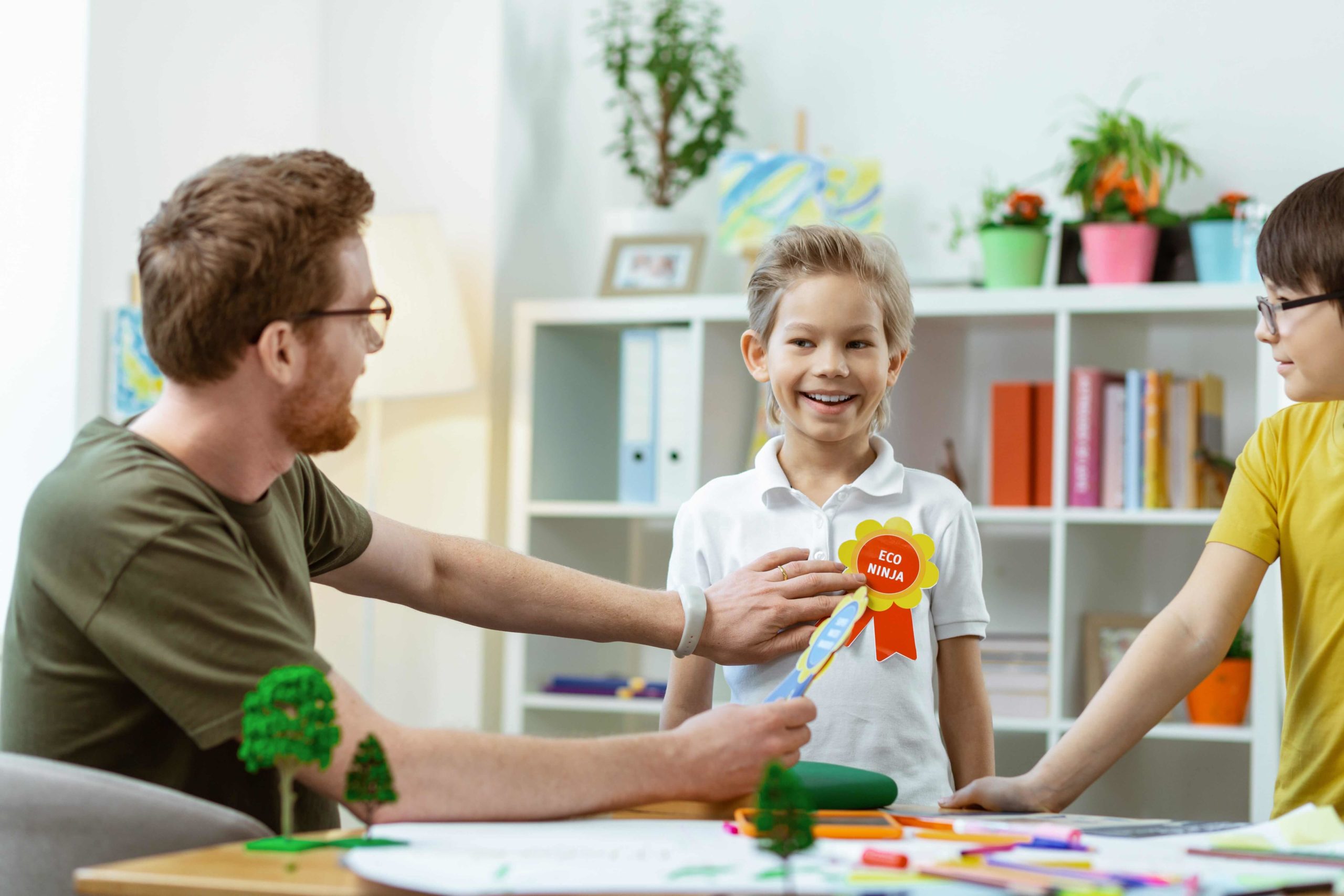 Teacher giving student a ribbon that says "Eco ninja" for his good work.