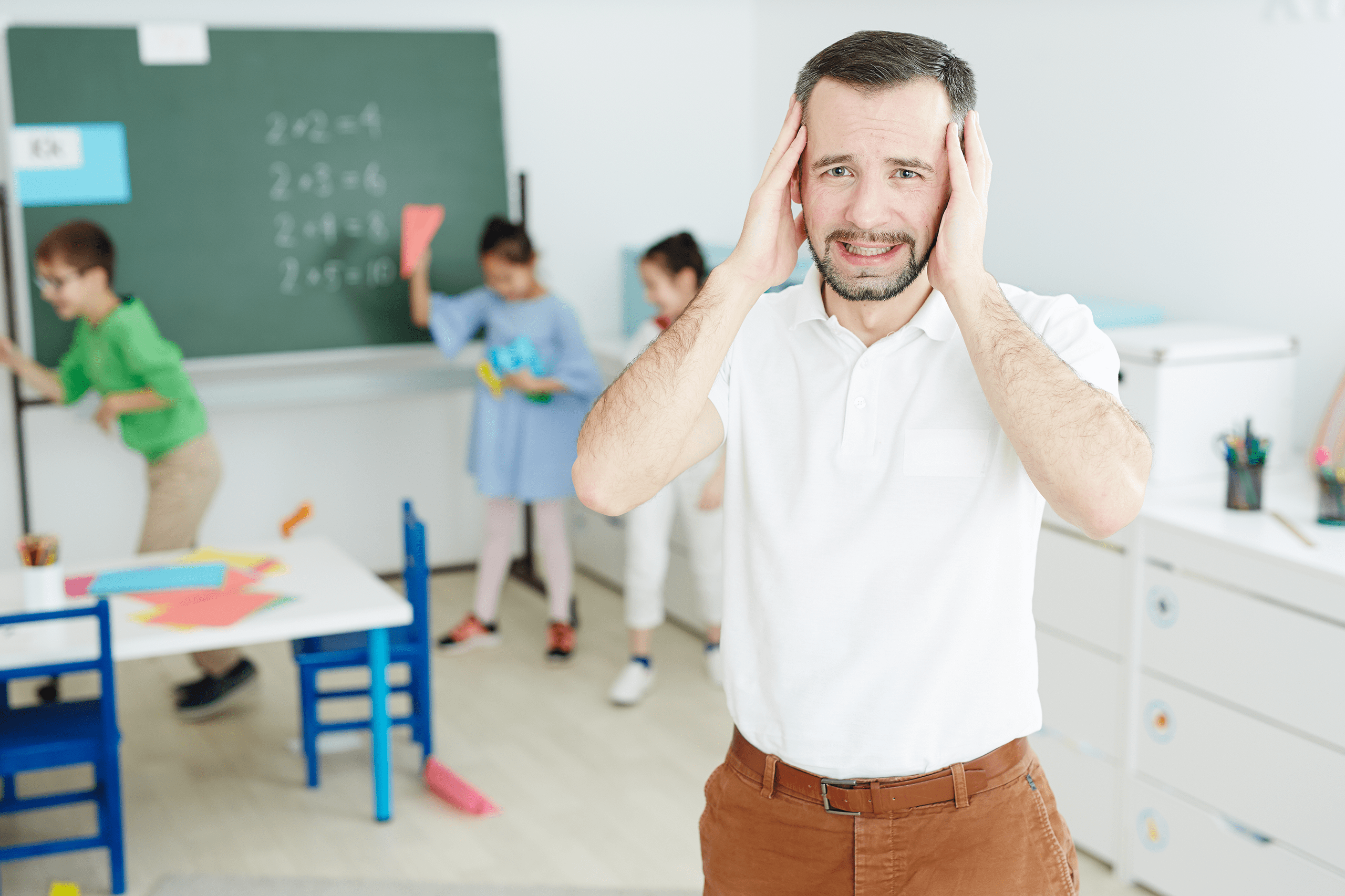 Frustrated male teacher looks worried while his students play with paper airplanes in the classroom.