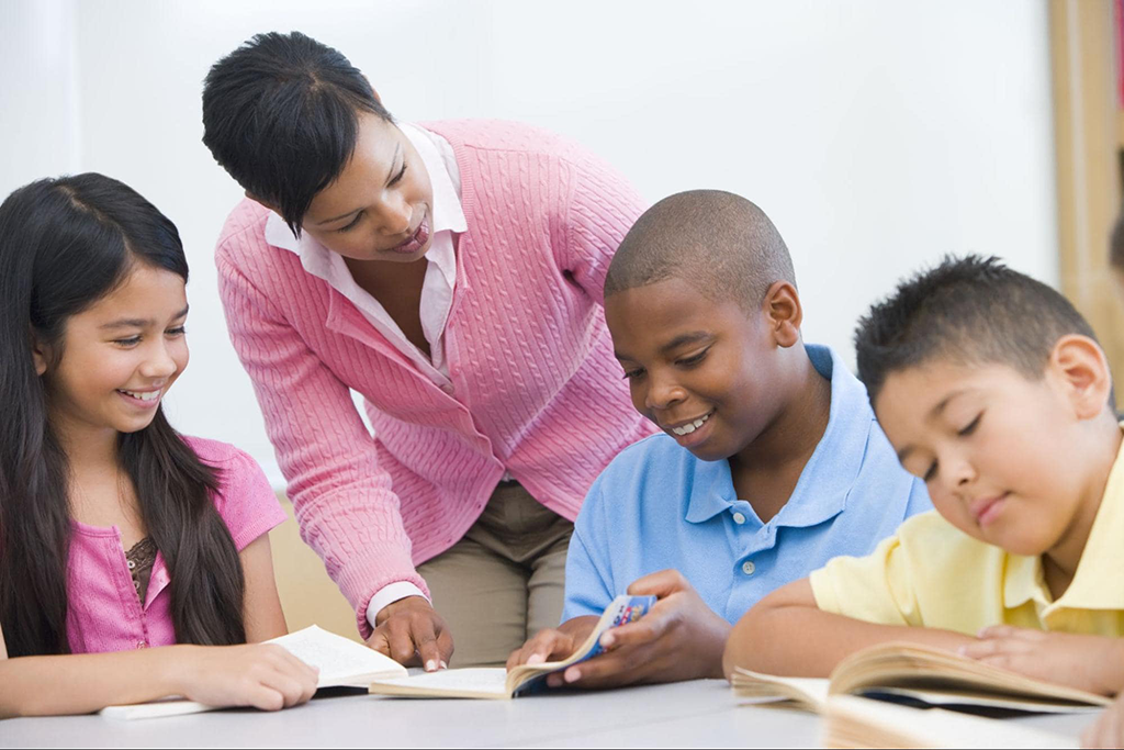 Female teacher helping group of three middle school students reading.