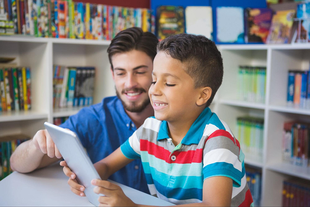 Male teacher points to words on iPad for elementary school boy.