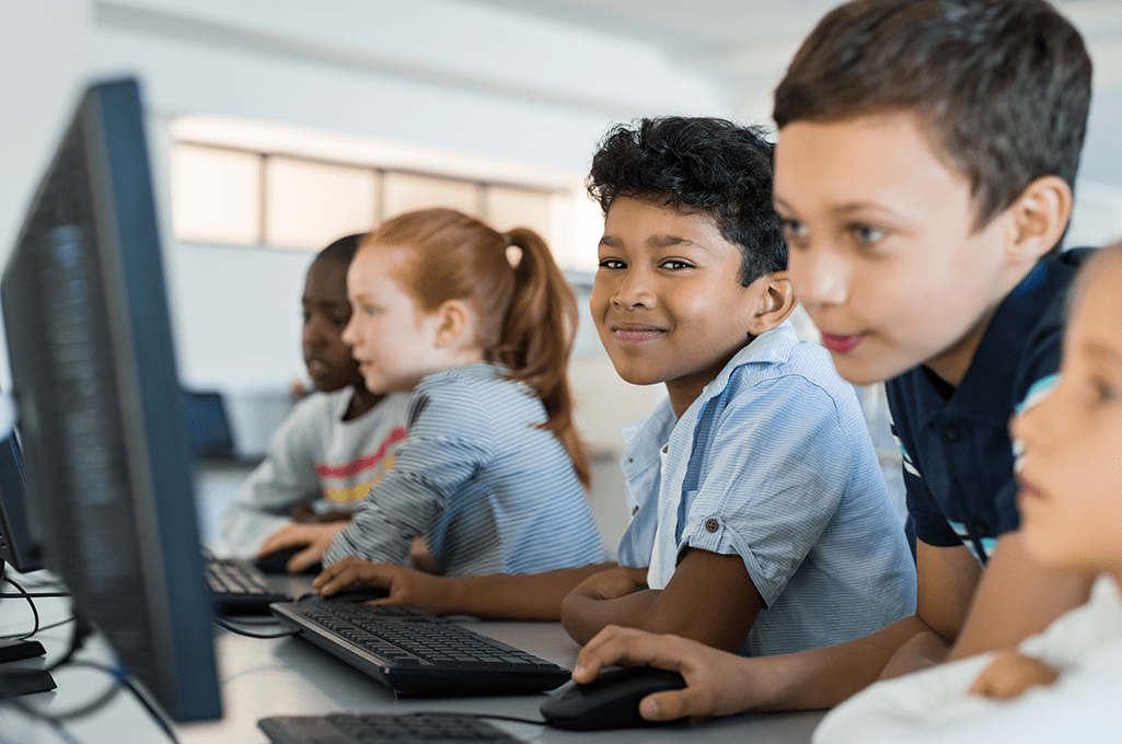 Group of five elementary school students using desktop computers at school.
