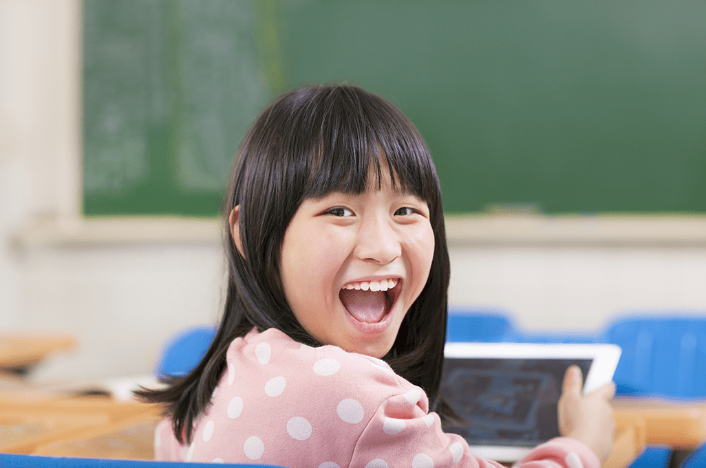 Elementary school girl smiles as she uses an iPad at her desk.