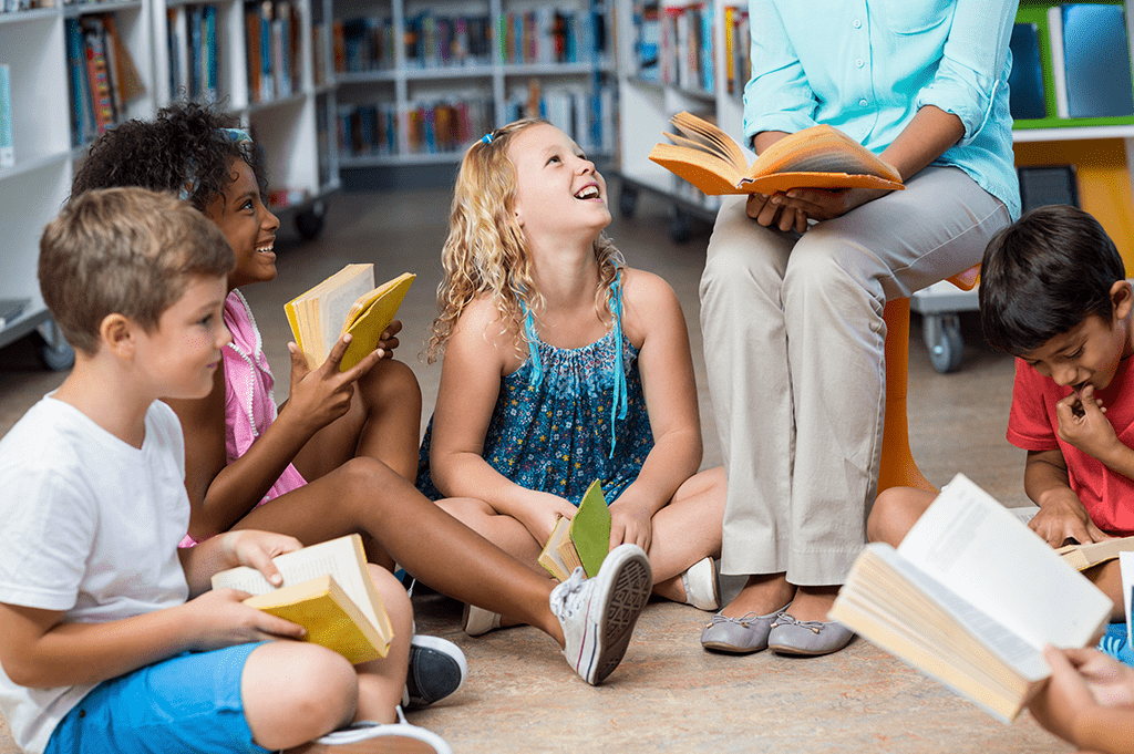 Two young girls smile up at female teacher during an interactive read aloud.