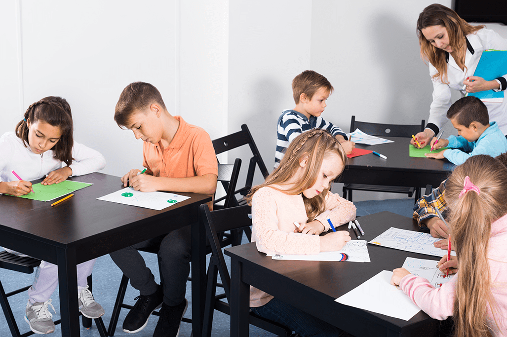 Group of intermediate students drawing at tables in a classroom.