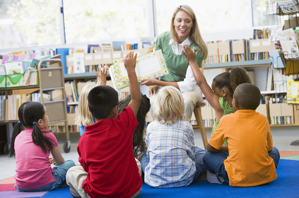 Female teacher reads aloud to elementary students sitting on the carpet.