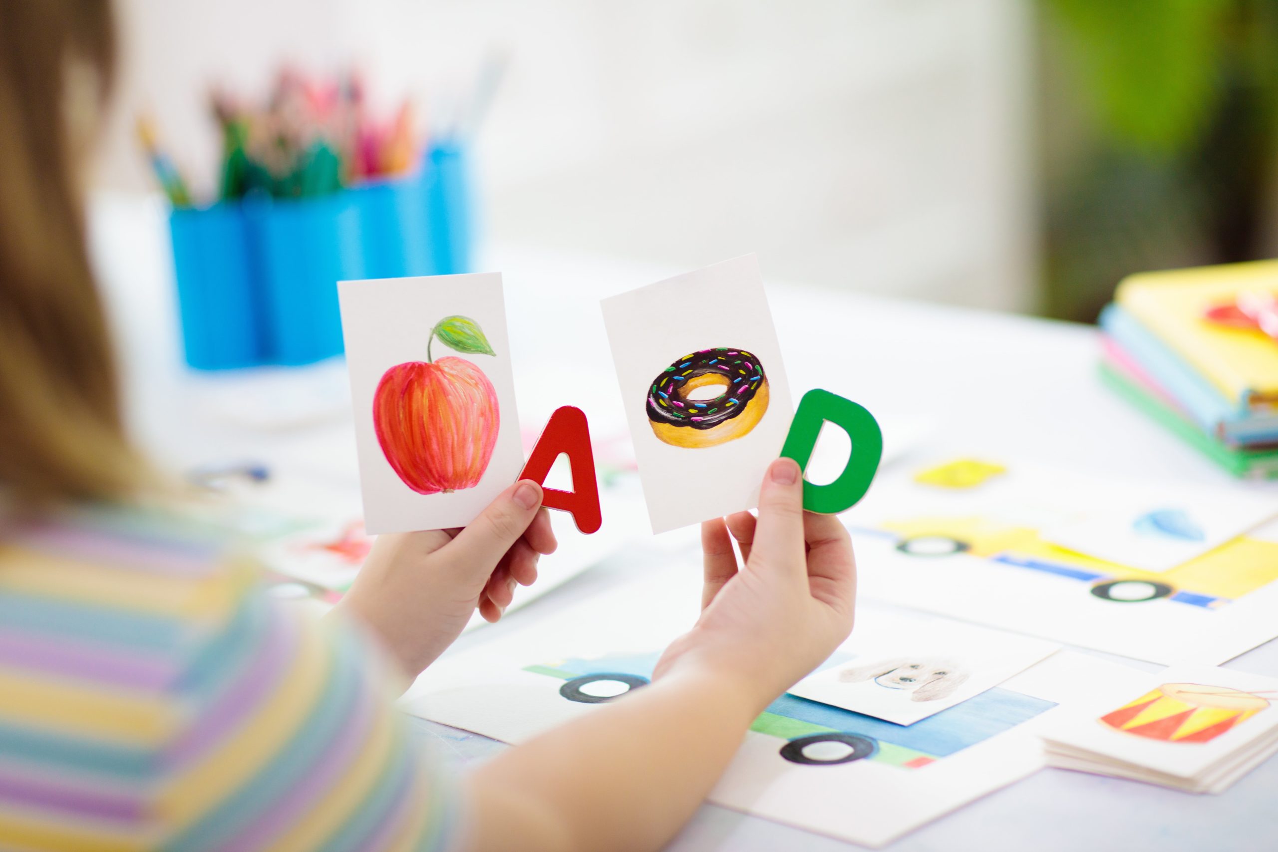 A person holding the letters A and D next to a picture of an apple and a donut.