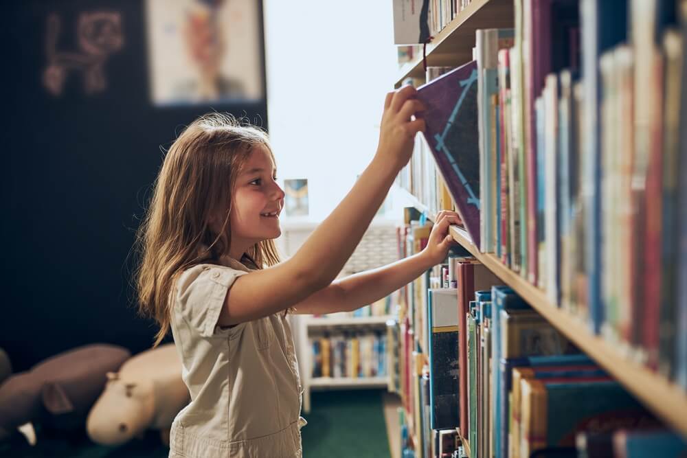 Little girls pulling a book off a shelf in a library.