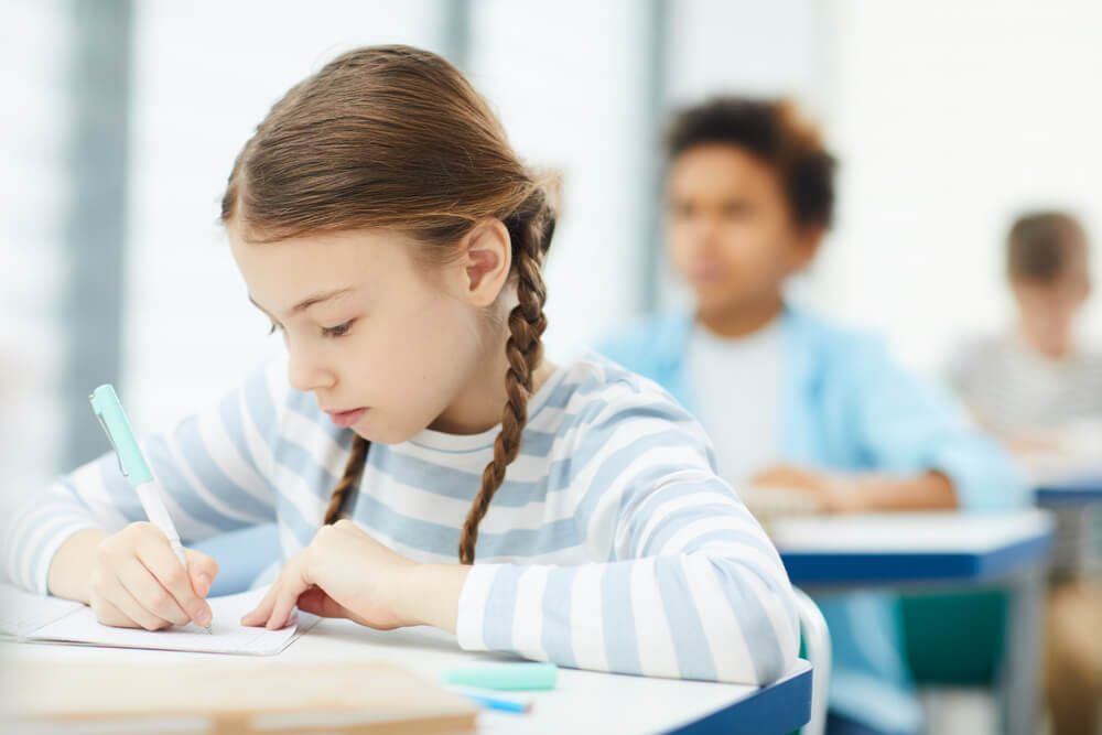 Little girl at a school desk writing in a notebook