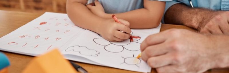 Little girl coloring at a table with male teacher