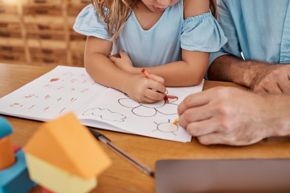 Little girl coloring at a table with male teacher.