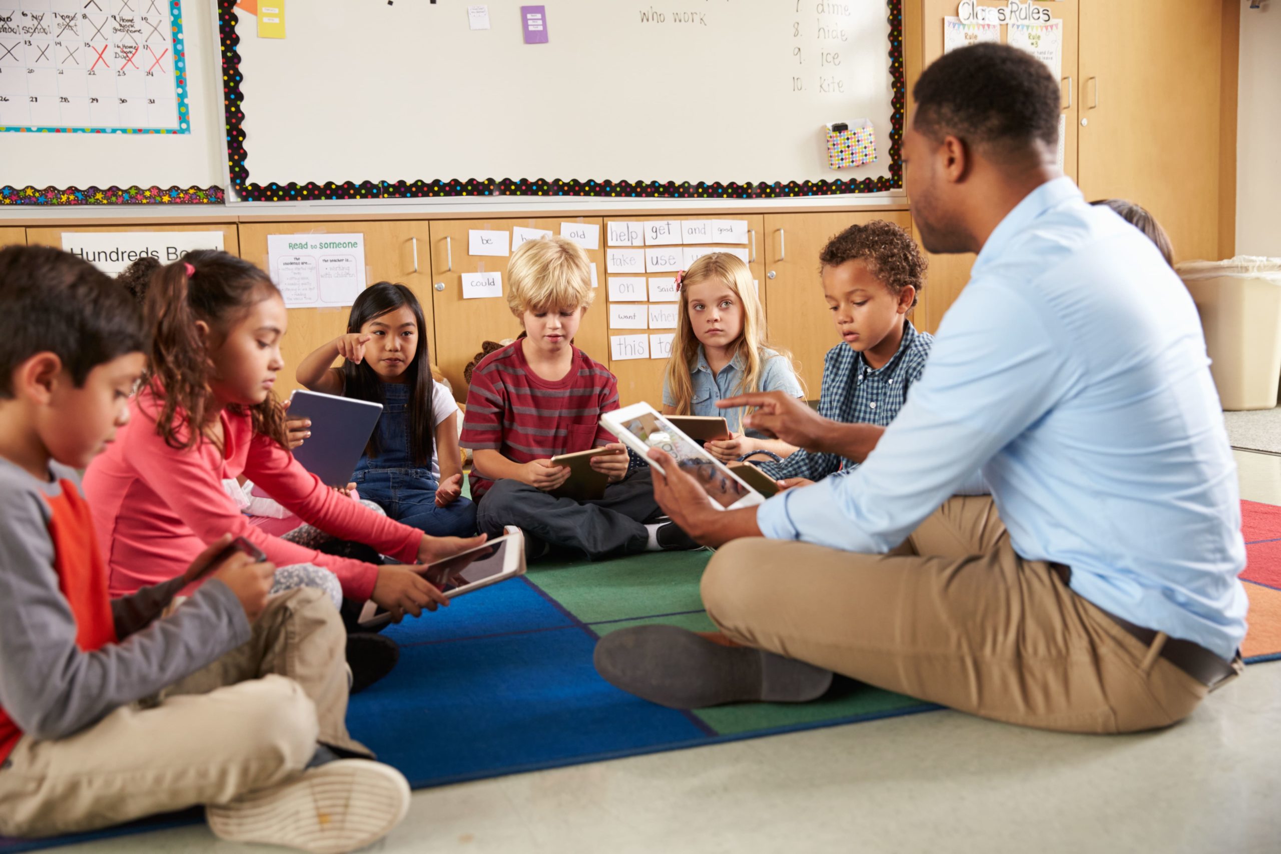 A teacher sitting on the floor with a group of students in a semicircle.