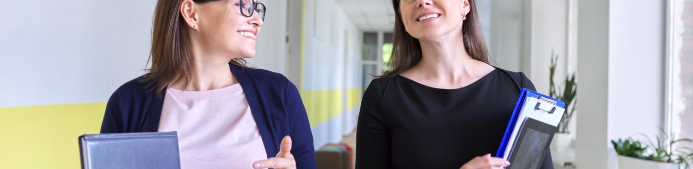 Two female co teachers walking down a school hallway.