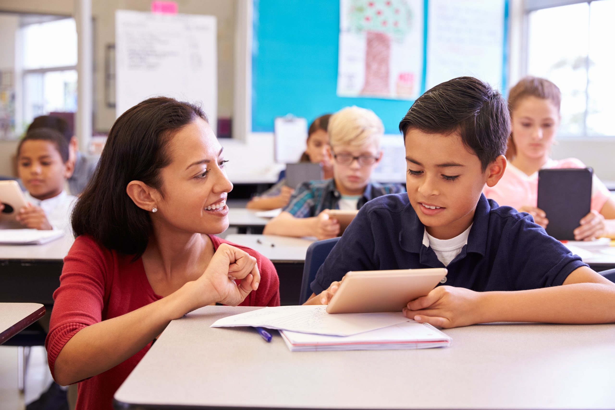 A male student asking a female teacher for help at his desk.