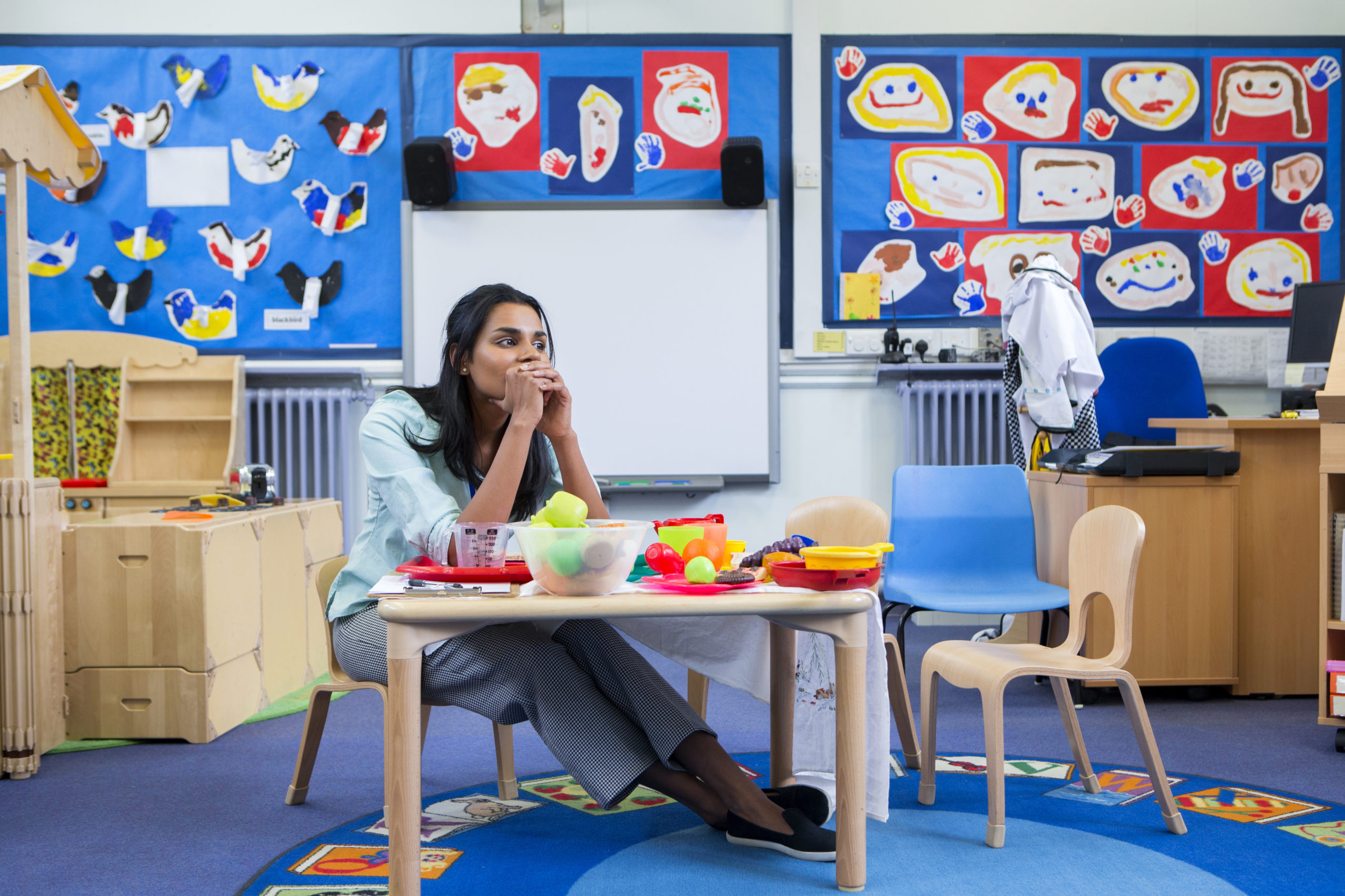 A stressed out teacher sitting at a small child's desk in her classroom.