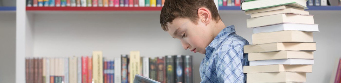 Young boy reading a stack of books.