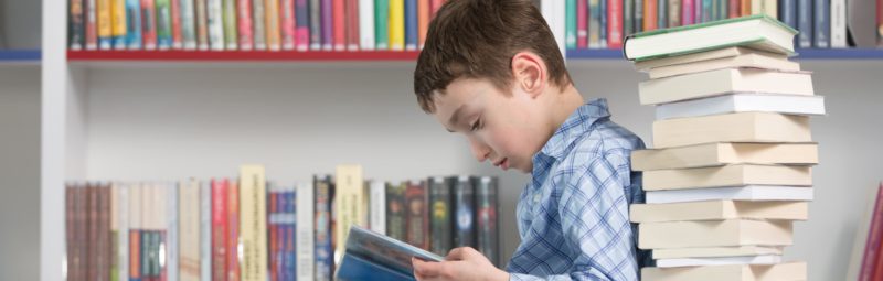 Young boy reading a stack of books.