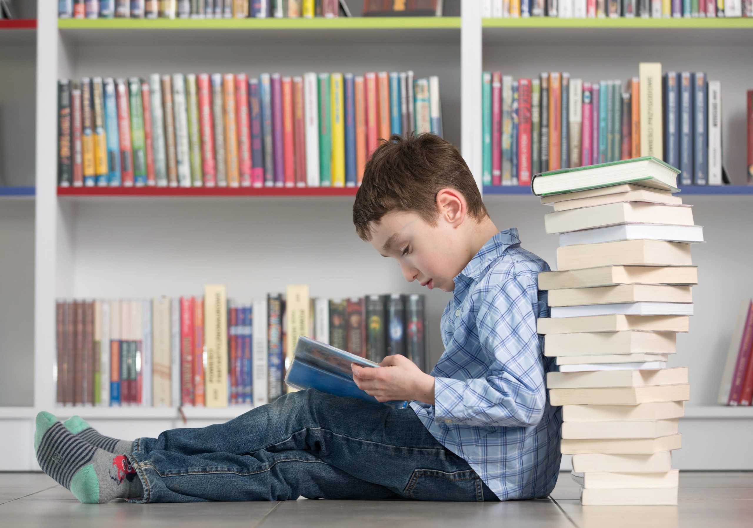 Young boy reading by a stack of books.