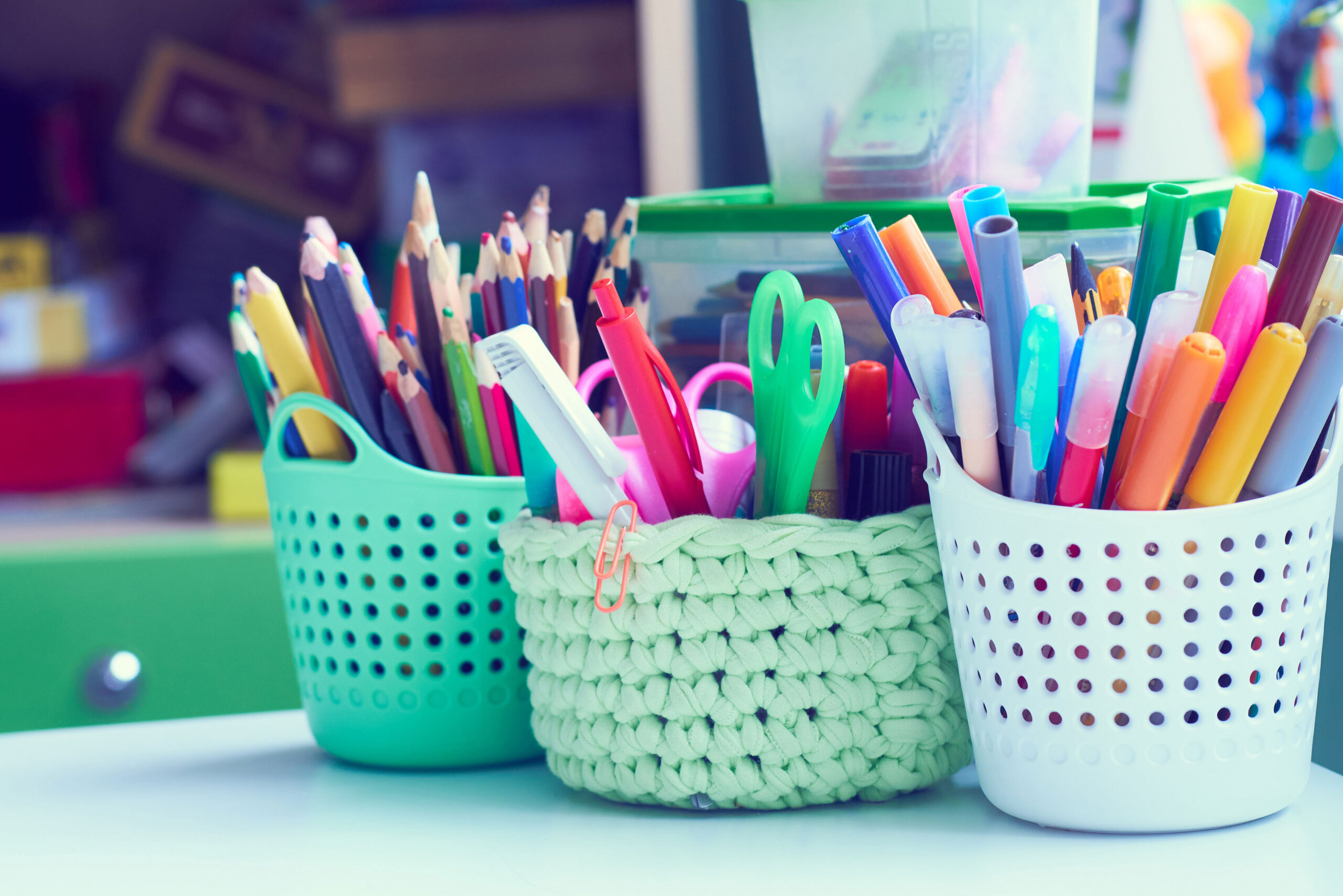 Classroom art supplies sit on a desk (colored pencils, scissors, markets, paper clips, etc.) inside cute buckets.