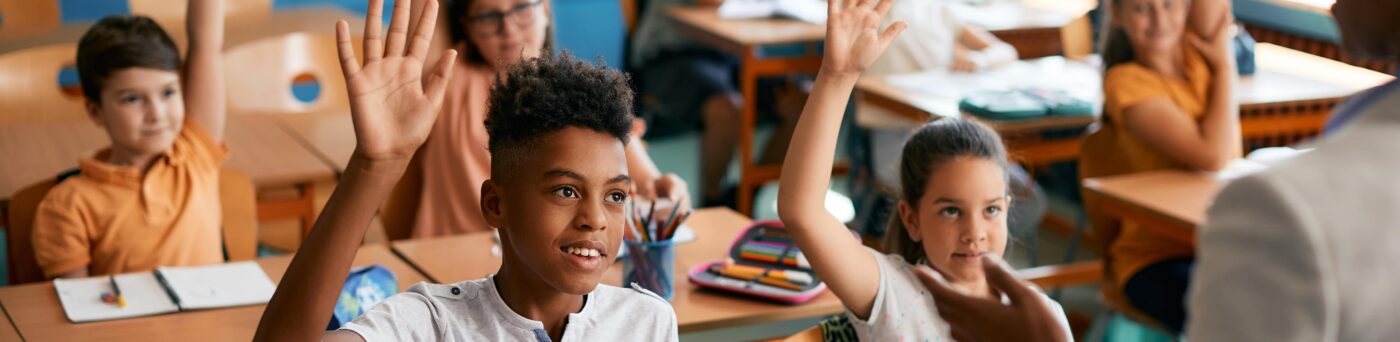 Students raising their hands at their desks.