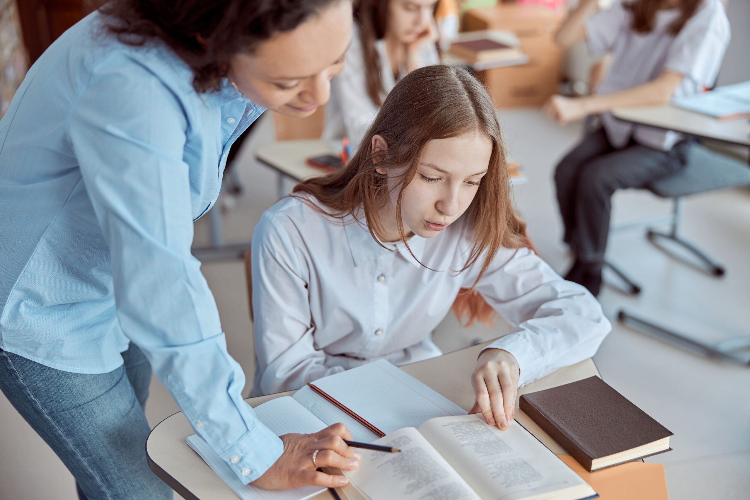 Teacher helping middle school student at her desk.