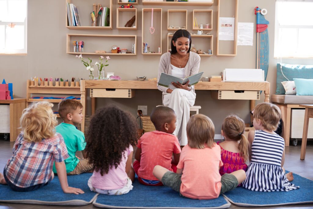 Elementary teacher reading to a group of 7 students sitting on a carpet.