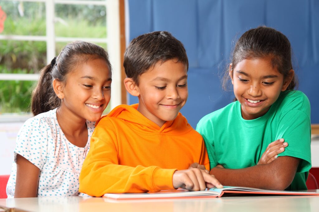 Three students reading a book together at their desk.