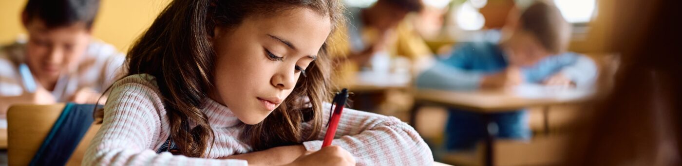 Elementary student writing on a paper at her desk.