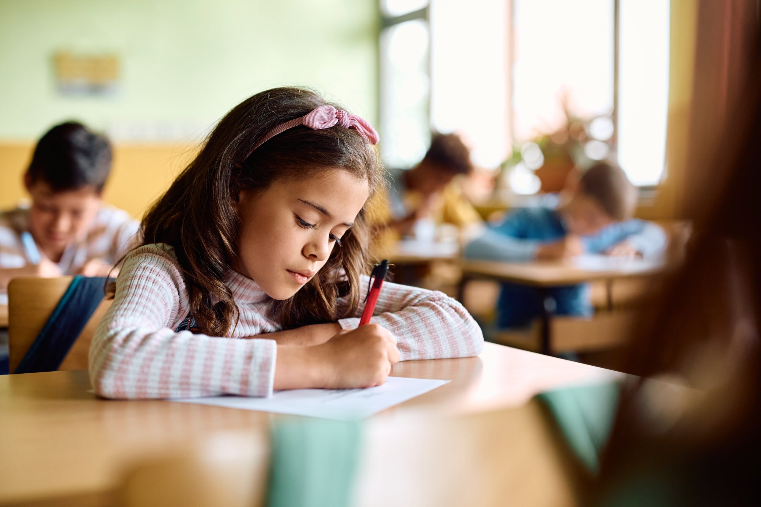Elementary student writing on a paper at her desk.