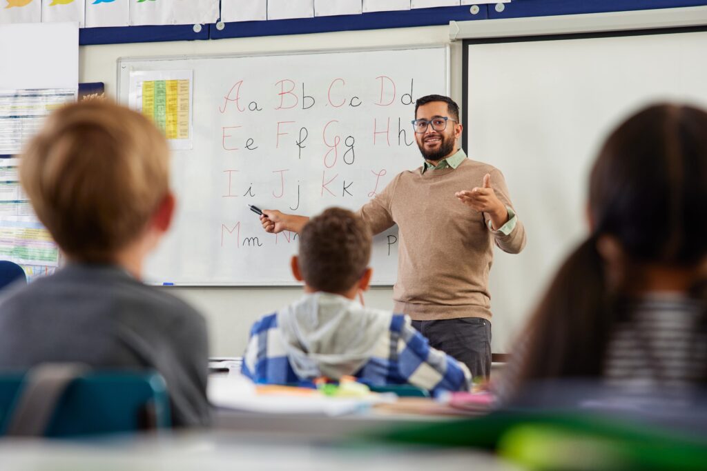 Teacher standing in front of the class teaching the alphabet to students.