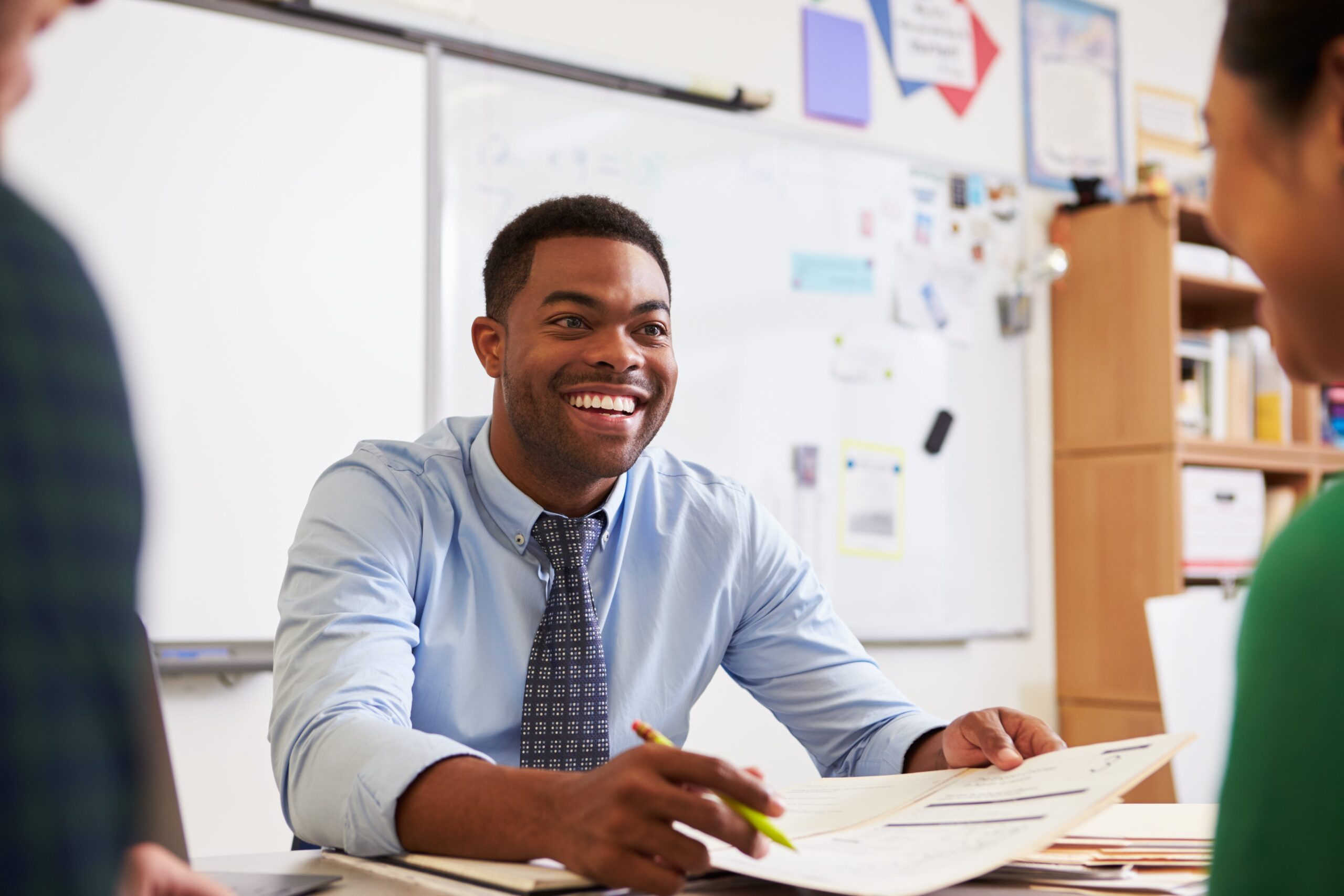 Teacher talking to colleagues at his desk.