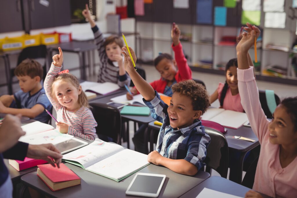 Students raising their hands in class. Some children are pointing in the air.