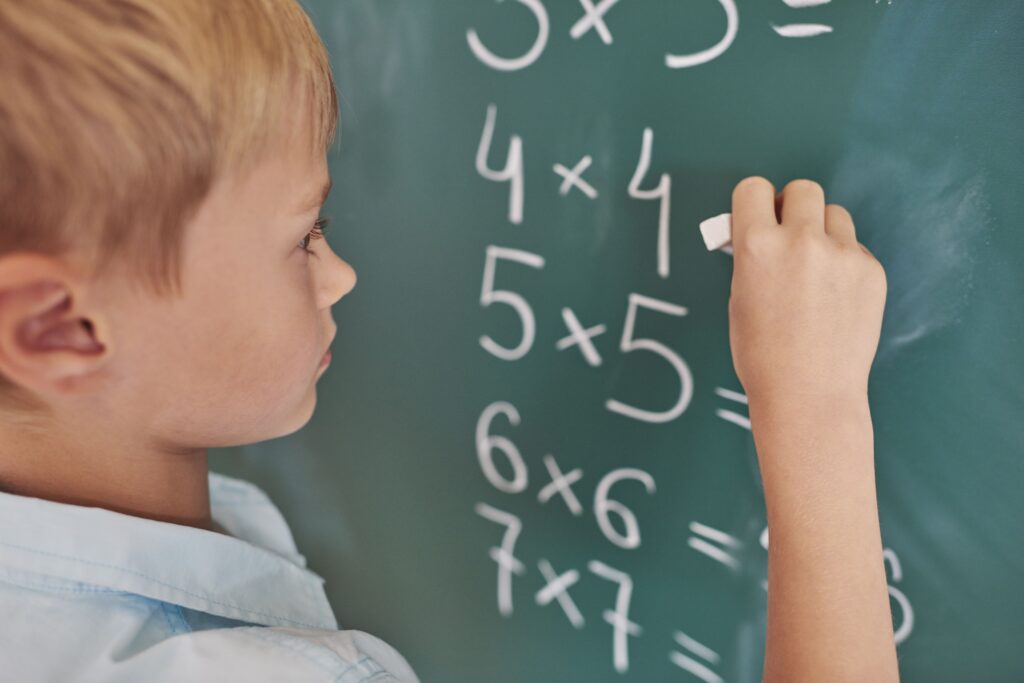 Young boy doing multiplication problems on a chalkboard.