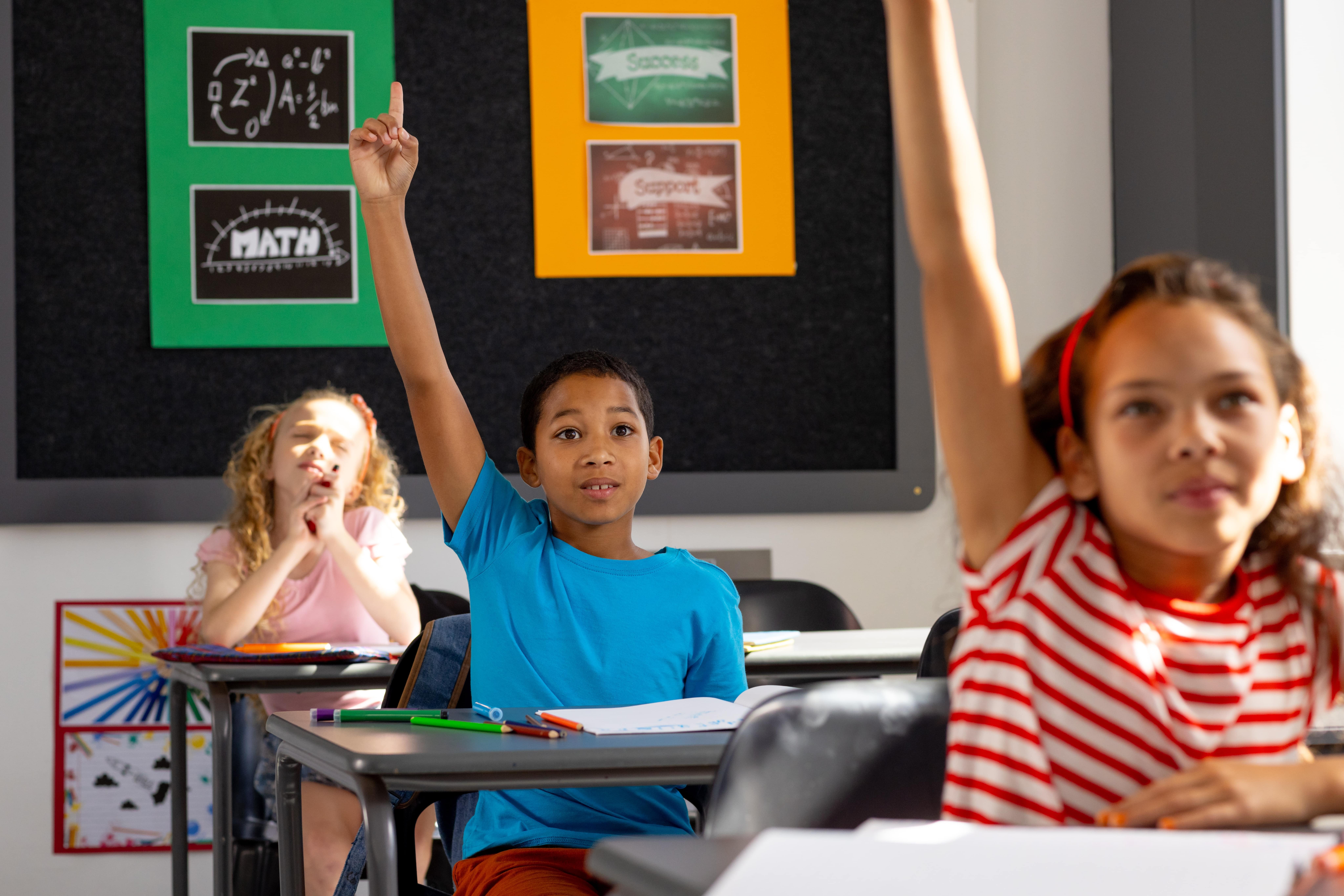 Students raising hands in a classroom to answer a question.