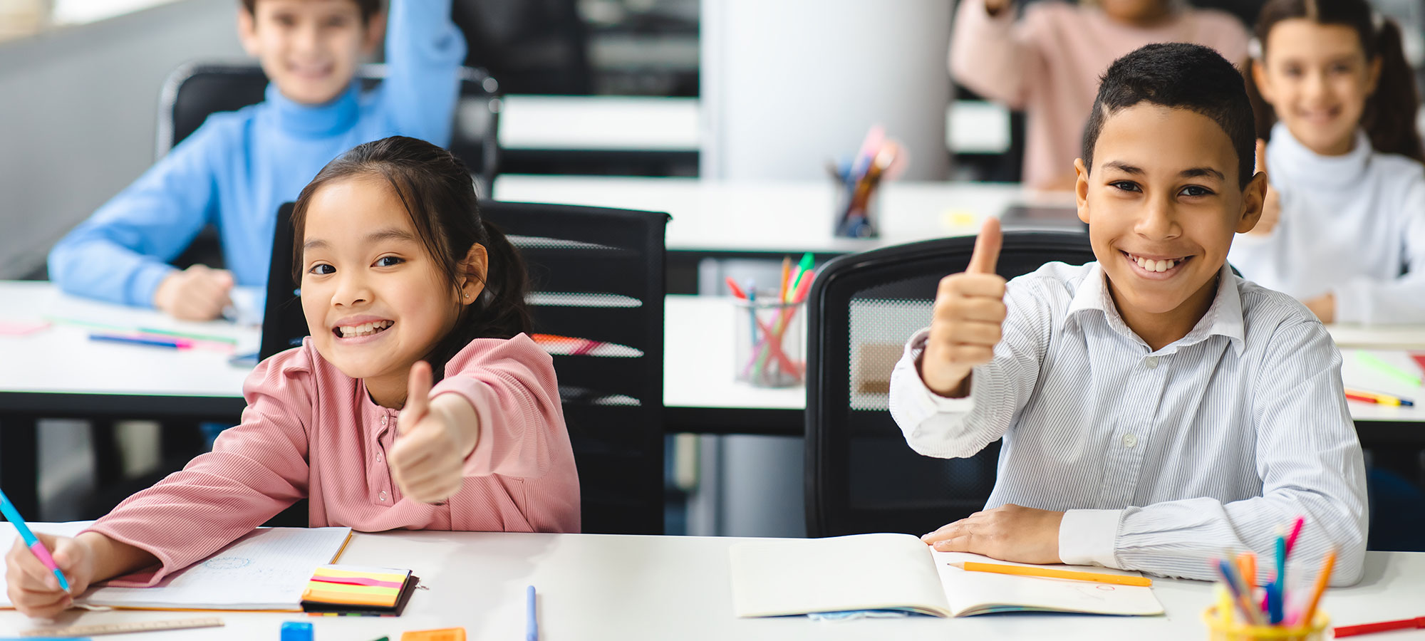 A diverse group of smiling students give a thumbs up.
