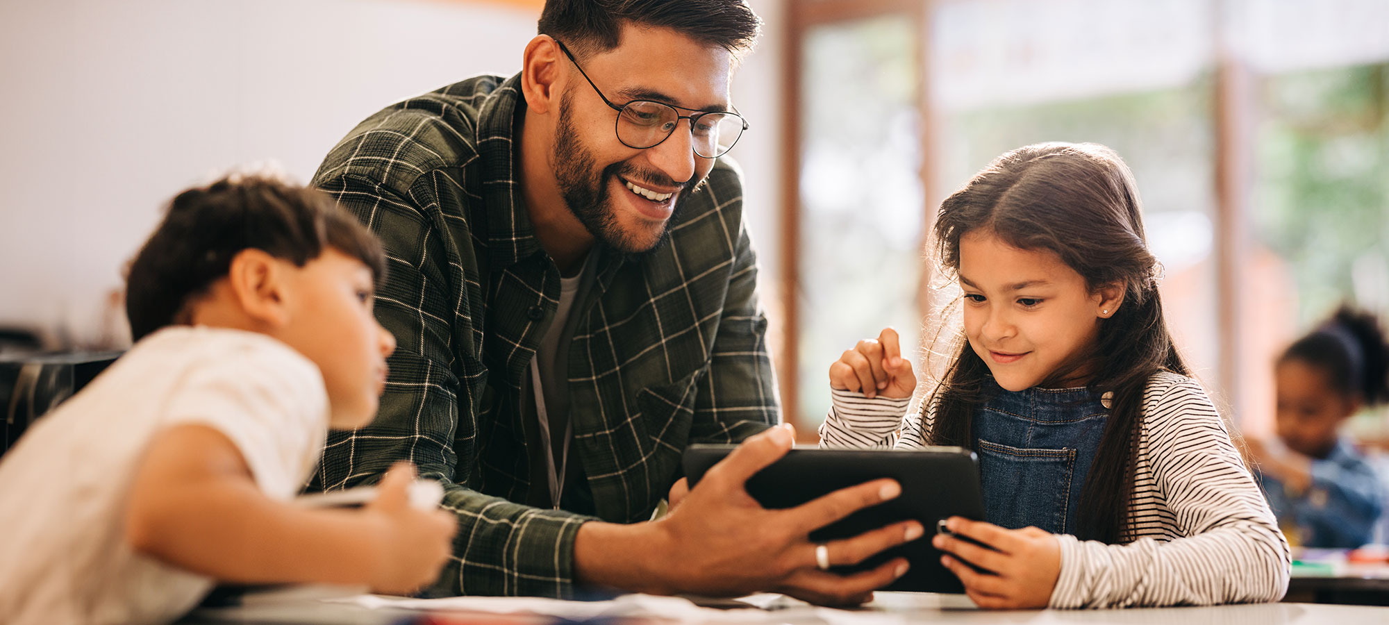 A male teacher holding an iPhone for two students to watch a video.