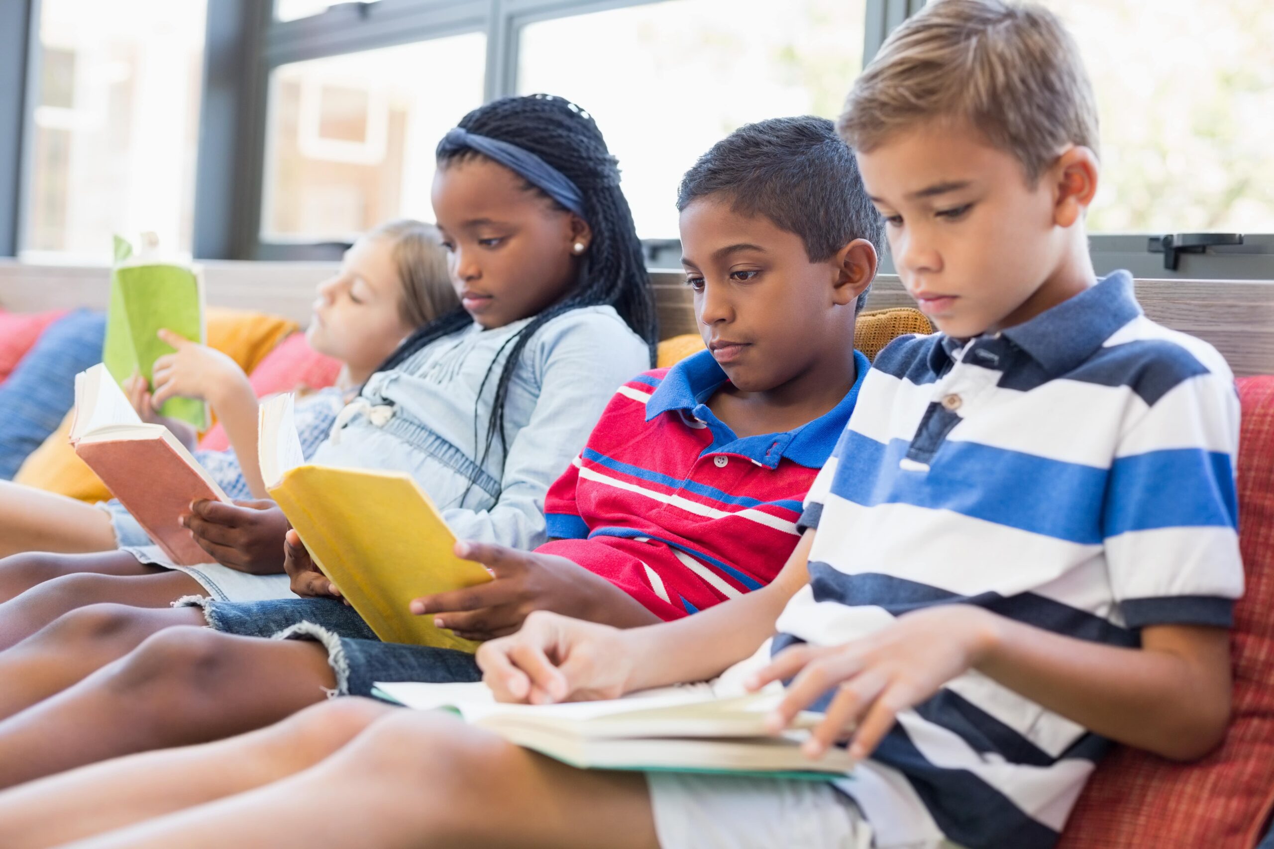 A group of students sitting on a comfy bench reading books silently.
