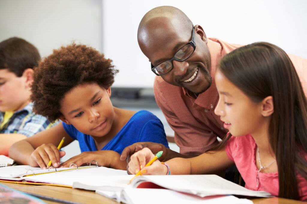 A male teacher helping two students learn English.